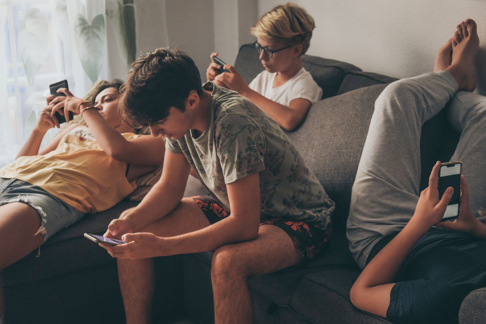 Group of teenager using smartphone sitting on a sofa at home. Young boys and a girl sharing photo and video watching social story online. Friends enjoying new trend technology.